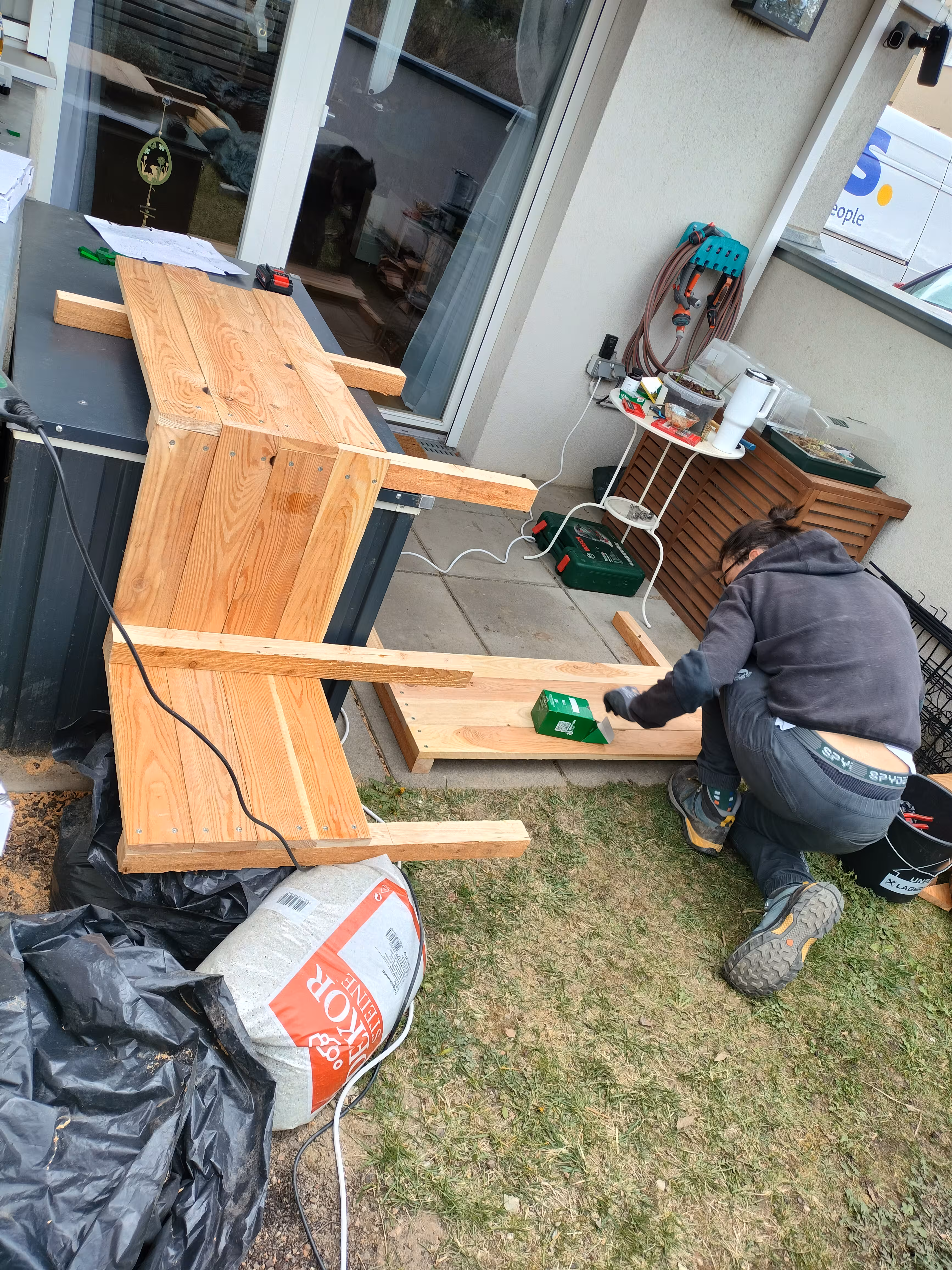 Dominik kneeling on the ground screwing together a side wall of the planter. Next to him is the rest of the planter resting on the toolbox